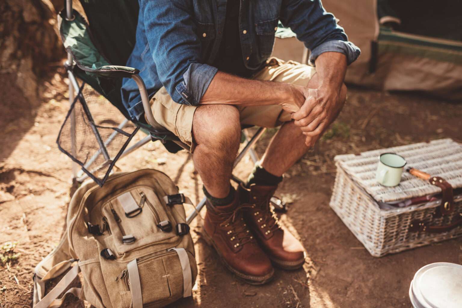 Close up shot of mature man sitting on a chair. Man relaxing at campsite, focus on hands.